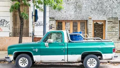 Camioneta clásica verde estacionada en calle con árboles y edificios